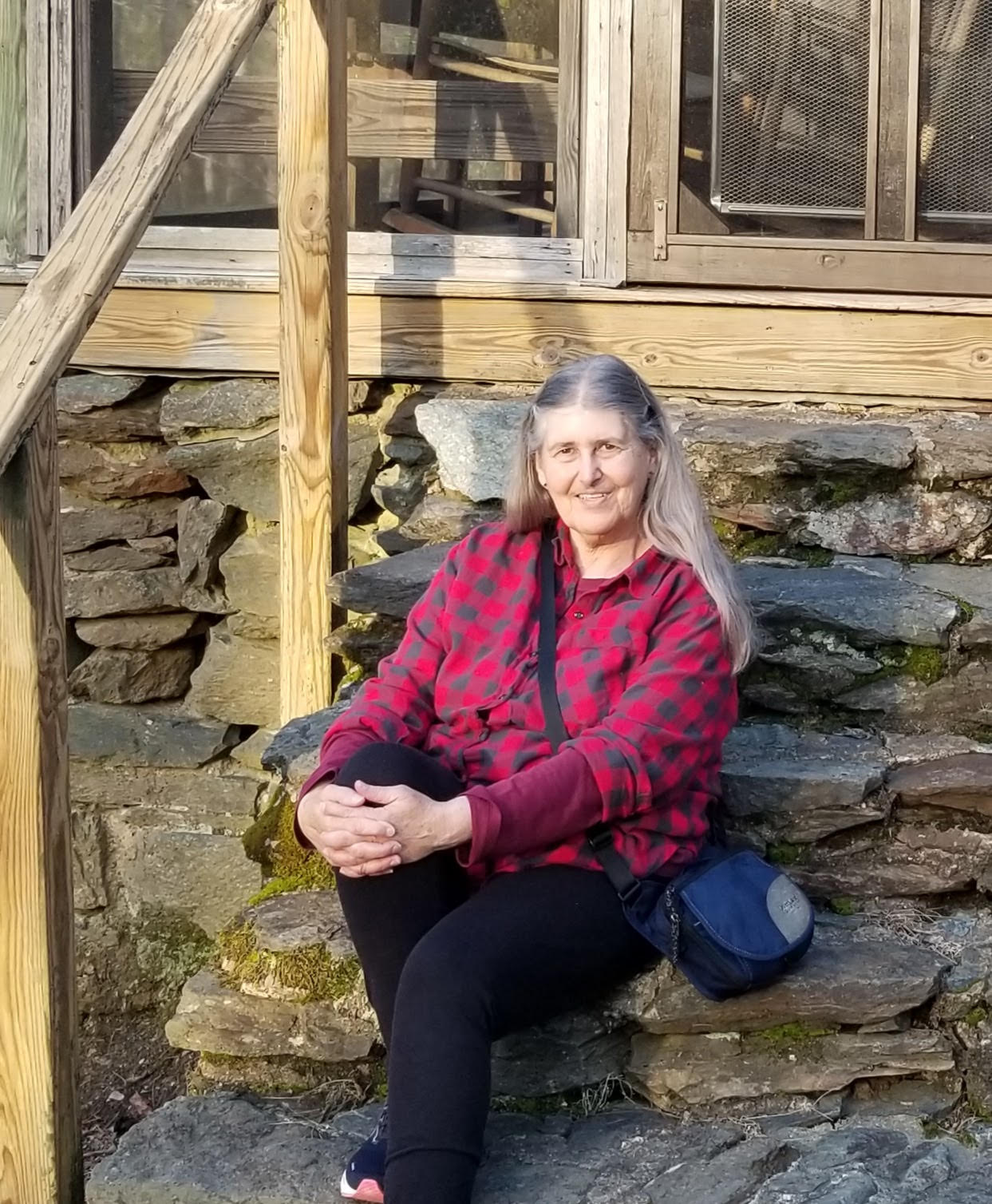 Person sitting on rustic stone steps beside a wooden railing, wearing a plaid shirt