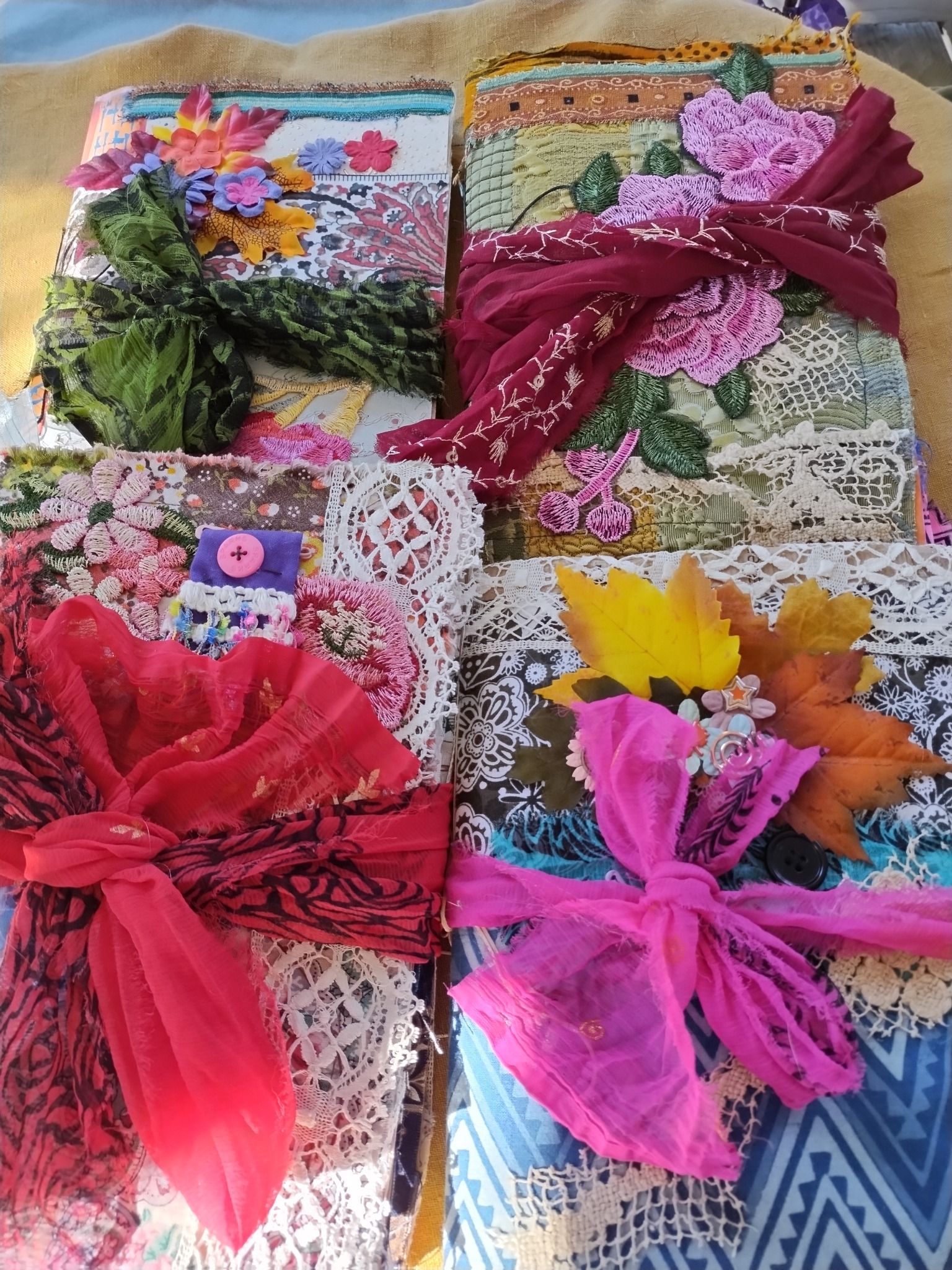 Four handmade journals wrapped with lace and colorful ribbons, featuring floral and leaf embellishments