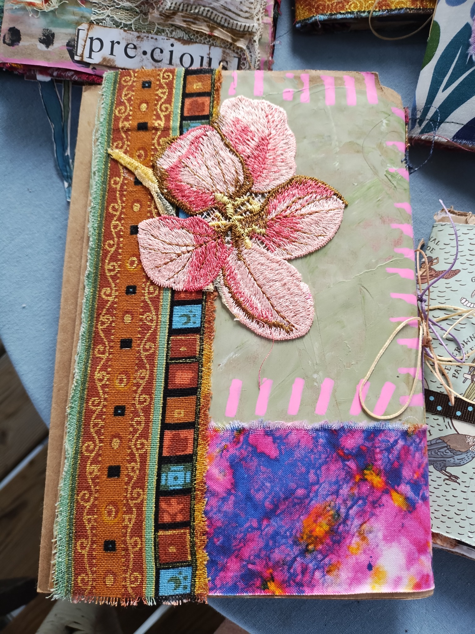 Handmade journal cover decorated with an embroidered pink flower and patterned fabrics